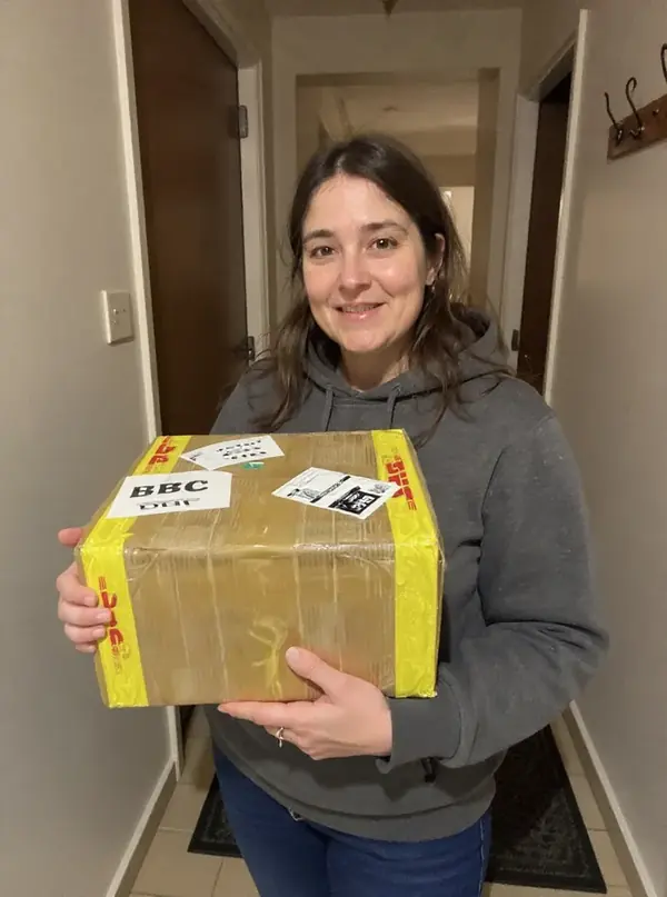 Mujer joven con la caja de su pedido importado en la entrada de su casa